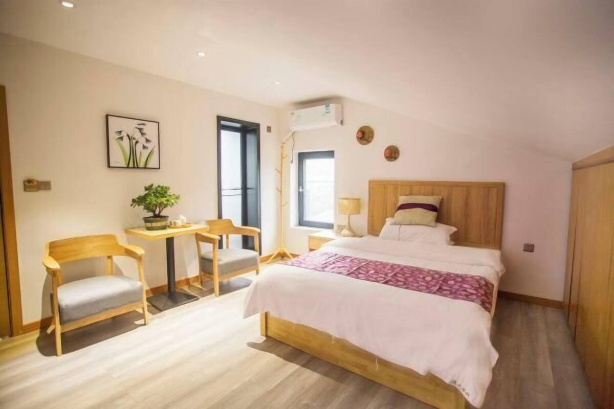 Un dormitorio con cama, escritorio, dos sillas, planta en maceta y ventana.