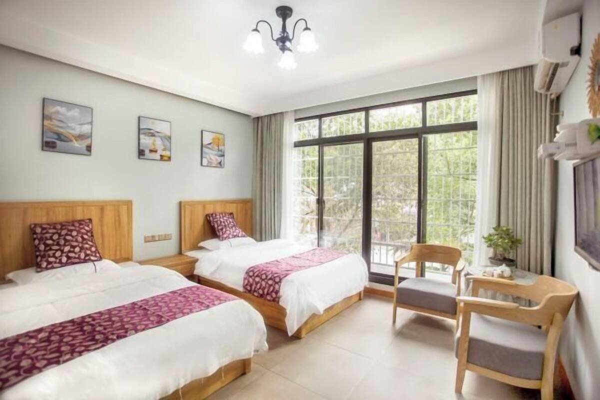 Habitación de hotel con dos camas, una silla, una mesa y un ventanal con vistas.