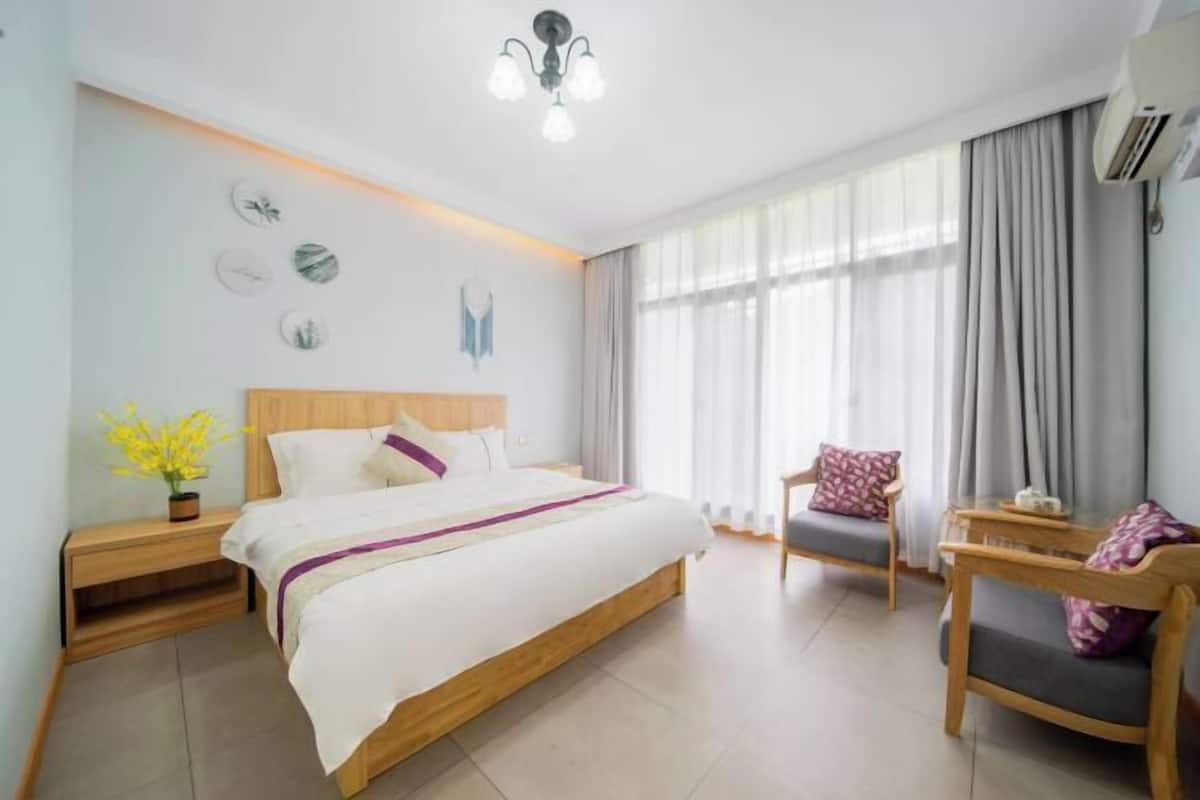 Un dormitorio con cama, mesita de noche, silla y ventana con cortinas.