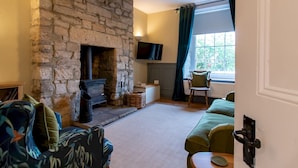 A cozy living room with a stone fireplace, comfortable seating, and a television mounted on the wall. - Charming Edwardian Stone Cottage Countryside Views - Pass the Keys (Stainton)