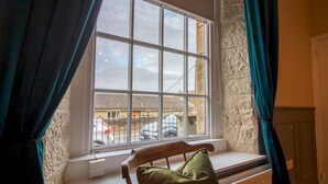 A room with a window overlooking a street, a chair with a cushion, and a stone wall. - Charming Edwardian Stone Cottage Countryside Views - Pass the Keys (Stainton)
