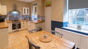 A modern kitchen with a wooden table, white cabinets, and a window with a view of stone steps. - Charming Edwardian Stone Cottage Countryside Views - Pass the Keys (Stainton)