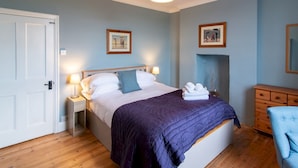 A bedroom with a bed, bedside tables, a nightstand, a dresser, a chair, and a wall-mounted lamp. - Charming Edwardian Stone Cottage Countryside Views - Pass the Keys (Stainton)