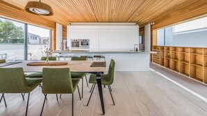 Une cuisine moderne avec des meubles blancs et des appareils en acier inoxydable, un coin repas avec des chaises à revêtement vert et un plafond en bois.