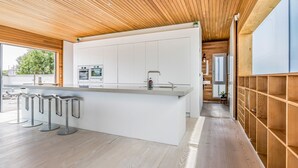 Une cuisine moderne avec des meubles blancs, un îlot central doté de tabourets de bar et des poutres en bois au plafond.