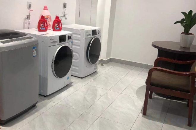 A laundry area with two washing machines, a drying machine, and a table with a potted plant.
