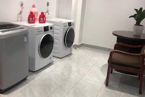 A laundry area with two washing machines, a drying machine, and a table with a potted plant. - Huating Hotel (Huzhou)
