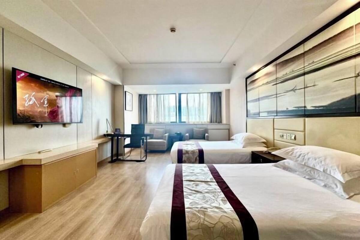 A hotel room with two beds, a TV, a desk, and a large window.