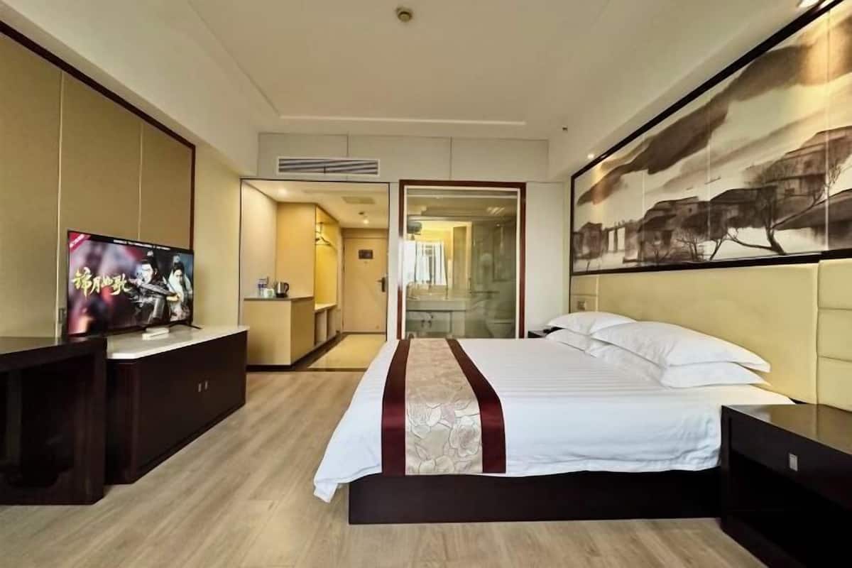 A hotel room with a bed, a TV, a desk, and a painting on the wall.
