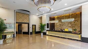 A hotel reception area with a marble floor, a reception desk, a chandelier, and a wall with a textured design.