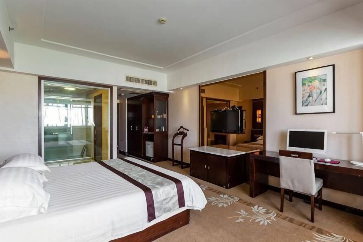 A hotel room with a bed, desk, TV, wardrobe, and a mirror.