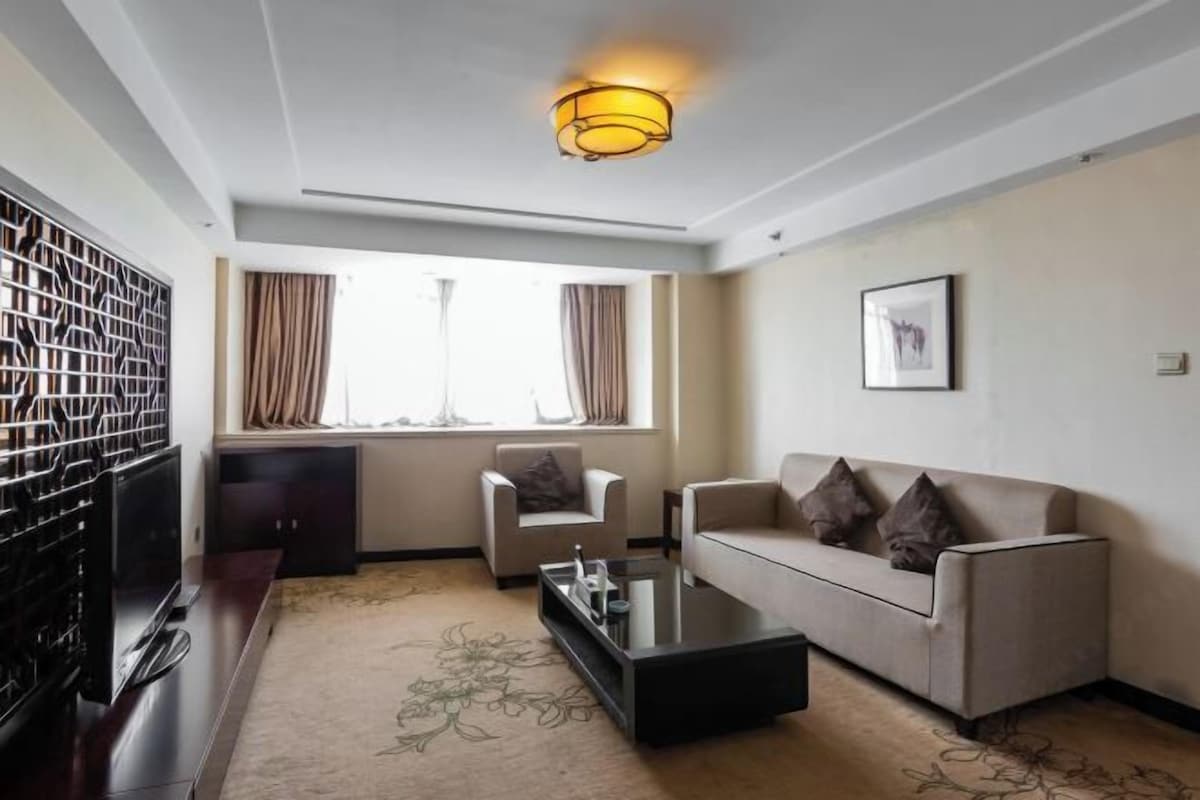 A modern living room with a sofa, armchairs, a coffee table, and a TV.