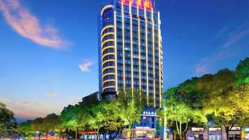 A tall hotel with a prominent sign at the top, surrounded by trees and other buildings.