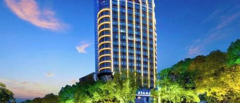 Un hotel alto con un letrero llamativo en la parte superior, rodeado de árboles y otros edificios.