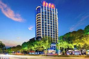 A tall hotel with a prominent sign at the top, surrounded by trees and other buildings. - Huating Hotel (Huzhou)