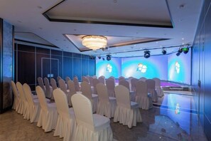 A conference room with rows of chairs, a stage with a blue backdrop, and a chandelier. - Huating Hotel (Huzhou)