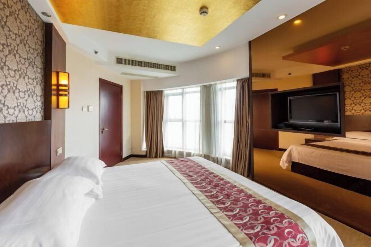 A hotel room with a large bed, a television, and a window with curtains.