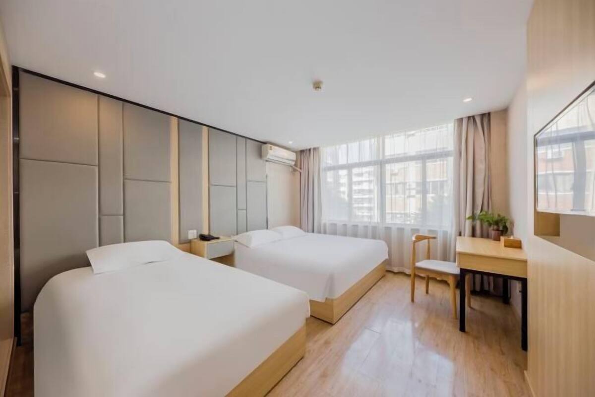 A hotel room with two beds, a desk, a chair, and a large window.