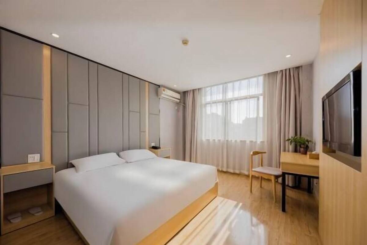 A modern hotel room with a large bed, a desk, a chair, and a TV.