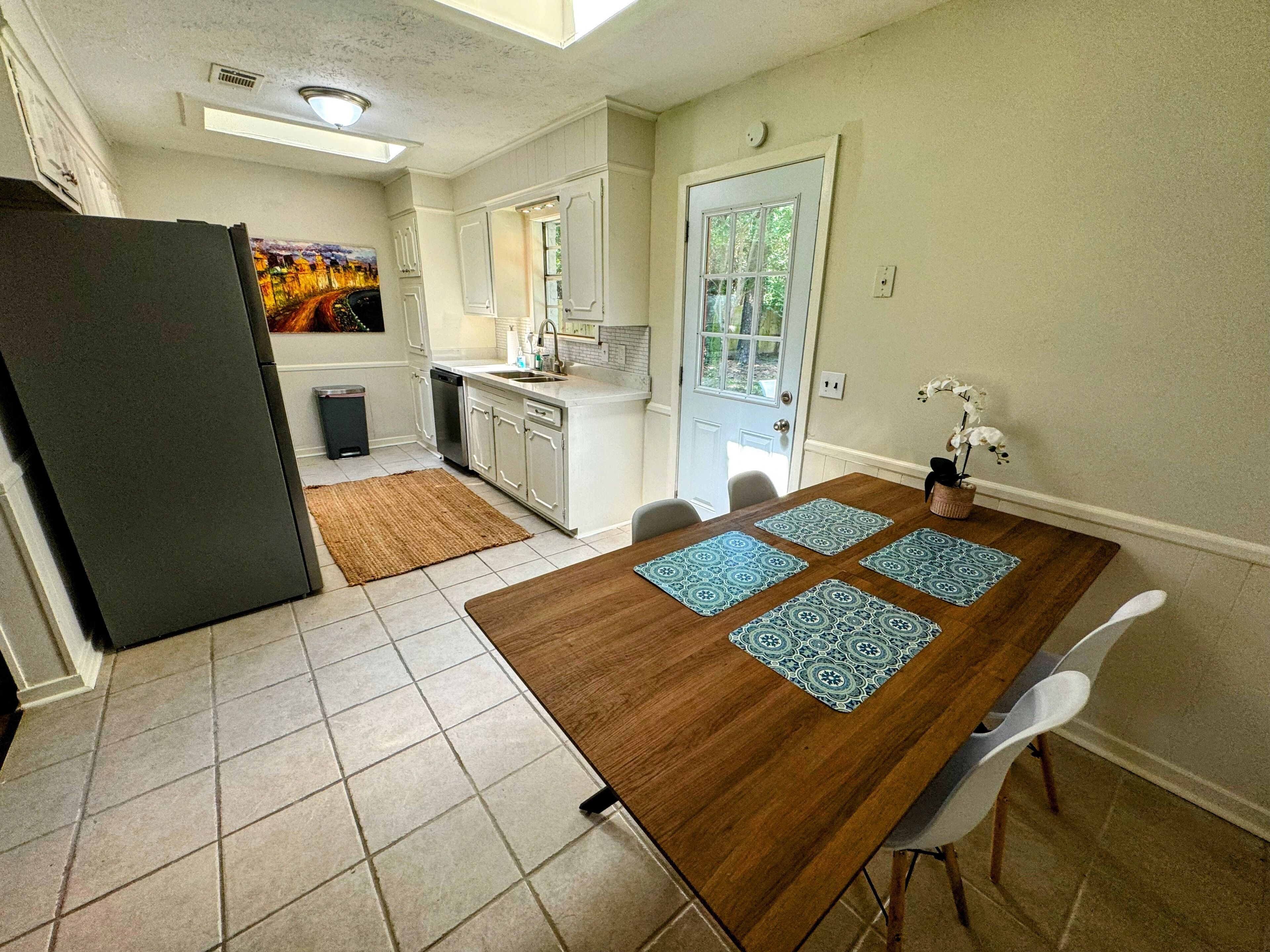 Een compacte keuken met witte kasten, een ingebouwde vaatwasser en een eethoek met een houten tafel en vier stoelen.
