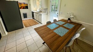 Eine kompakte Küche mit weißen Schränken, einem eingebauten Geschirrspüler und einem Essbereich mit Holztisch und vier Stühlen.