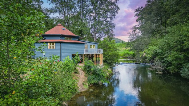 A blue house with a red roof, a deck, and a river in the background. - RiverFront Retreat/Fenced/LOVEDogsStayForFree/KingBeds/Sauna+SteamShower (Ellijay)