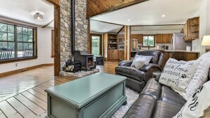 A spacious living area with a stone fireplace, leather sofa, and a view of the kitchen and dining area. - RiverFront Retreat/Fenced/LOVEDogsStayForFree/KingBeds/Sauna+SteamShower (Ellijay)