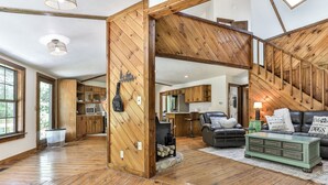 A spacious living area with a wooden floor, a black leather sofa, a green sideboard, and a kitchen in the background. - RiverFront Retreat/Fenced/LOVEDogsStayForFree/KingBeds/Sauna+SteamShower (Ellijay)