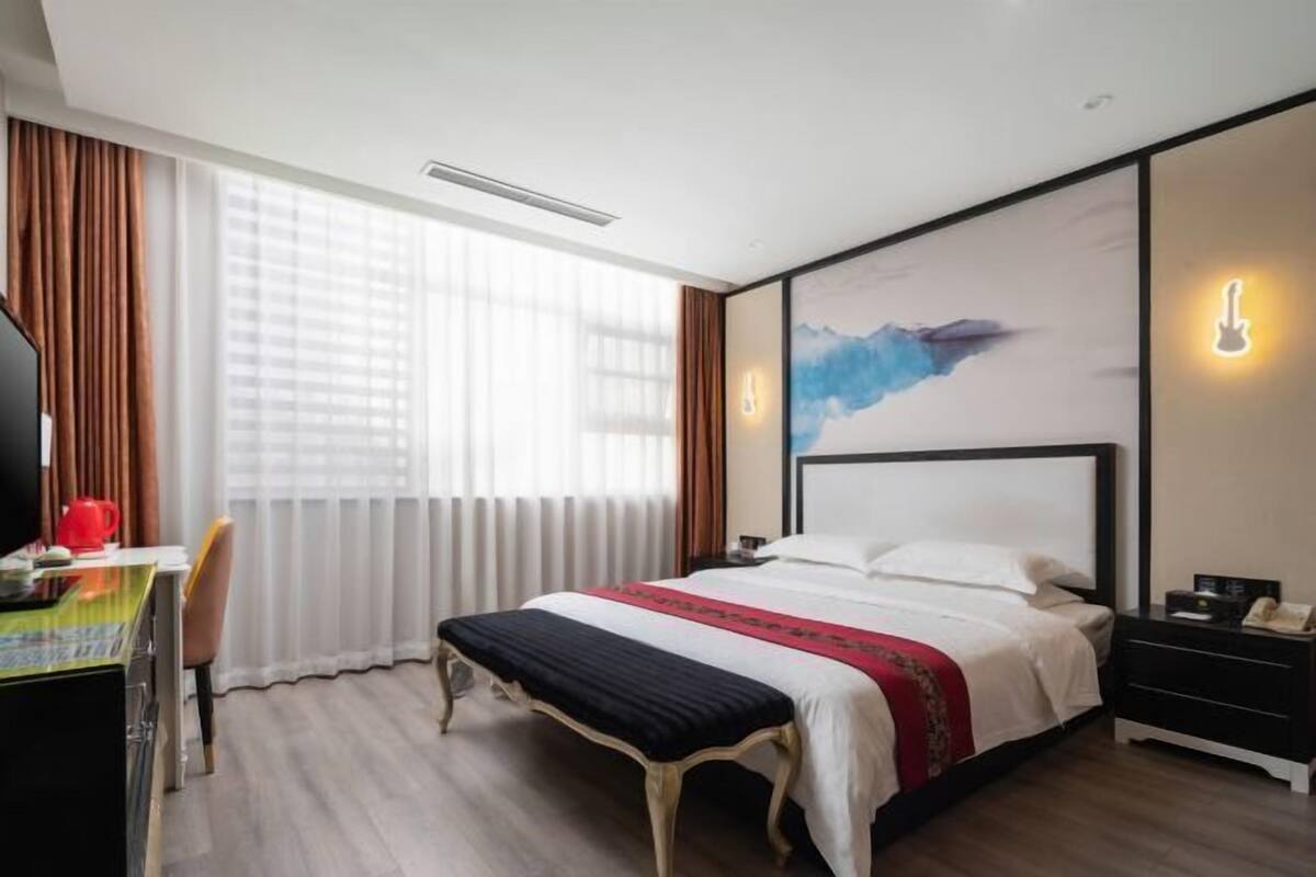 Hotellihuone, jossa on sänky, yöpöytä, lamppu ja työpöytä tuolilla.