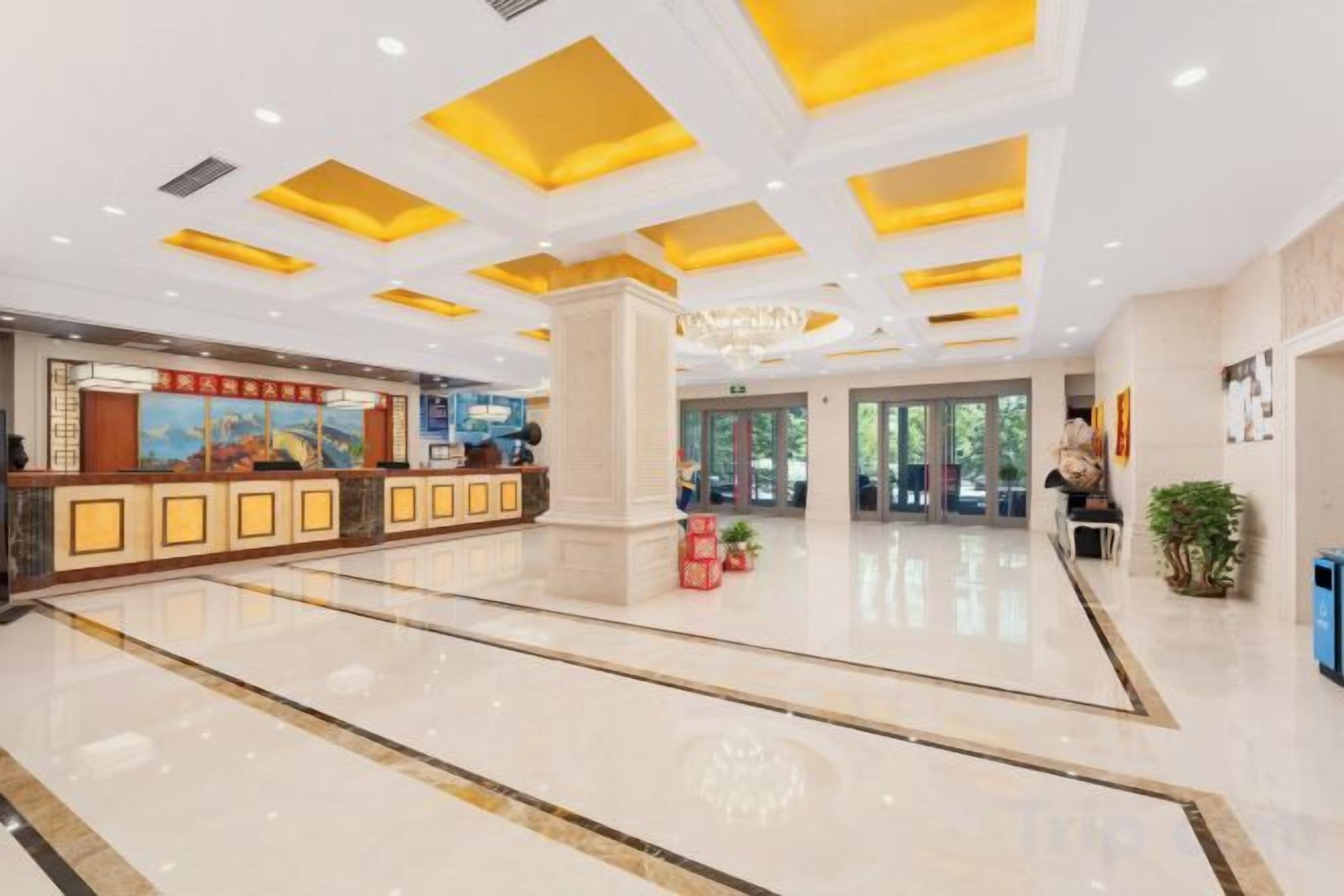 A hotel lobby with a reception desk, a large pillar, and a chandelier.