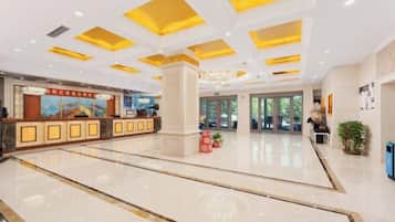 A hotel lobby with a reception desk, a large pillar, and a chandelier.