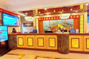 A hotel reception area with a marble counter, a television screen, and a large painting above the counter. - Shi Mao Garden Hotel (Beijing)
