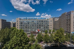 A multi-story building with a modern glass facade, surrounded by trees and parked cars. - Shi Mao Garden Hotel (Beijing)