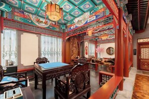 Quarto tradicional com mesa de madeira, cadeiras e teto decorativo.