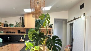 A modern kitchen with a black countertop, wooden cabinets, and a large island with a plant. - T-Street 3 Bed Beach Bungalow w/ Pool  (San Clemente)