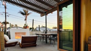 An outdoor patio with a fire pit, seating, and a glass door leading to a view of the neighborhood. - T-Street 3 Bed Beach Bungalow w/ Pool  (San Clemente)