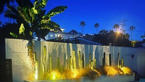 A swimming pool with a lighted cactus wall and palm trees in the background. - T-Street 3 Bed Beach Bungalow w/ Pool  (San Clemente)