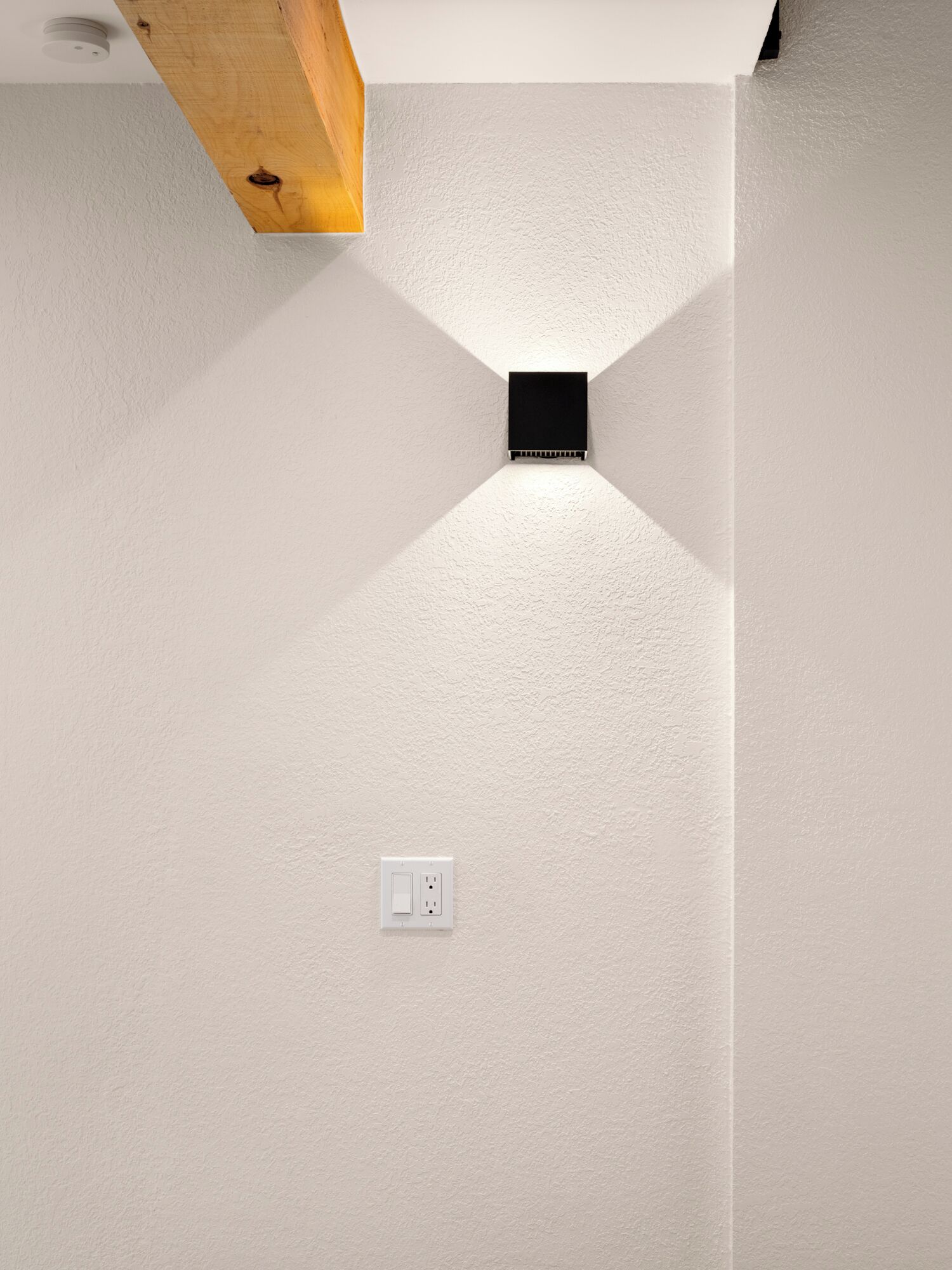 A white textured wall with a recessed light fixture and a white electrical outlet.