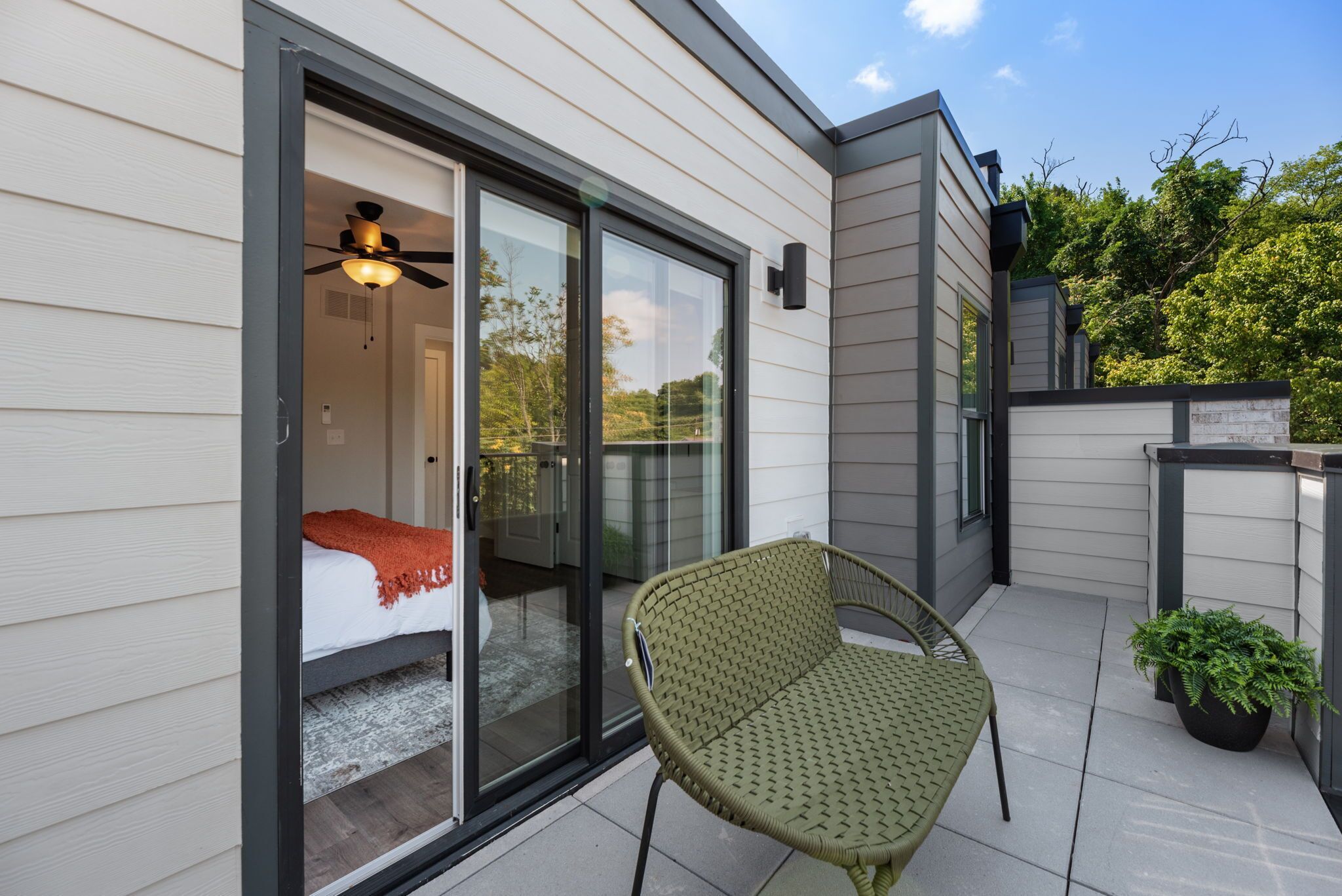 Une chambre avec un lit, un ventilateur de plafond et une porte-fenêtre coulissante donnant sur un balcon.
