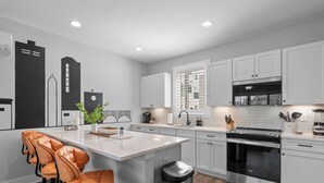 Una cocina moderna con gabinetes blancos, un horno de acero inoxidable y una isla central con taburetes de bar.