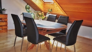 A dining area with a wooden table and black chairs, surrounded by potted plants and a wooden bench.