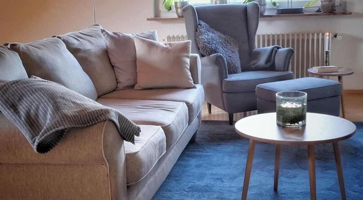 Een woonkamer met een bank, fauteuil en een ronde salontafel.