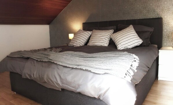 A bedroom with a large bed, dark headboard, and a patterned blanket.