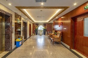 Un vestíbulo de hotel con suelo de mármol, paredes de madera, un mostrador de recepción y una zona de estar.
