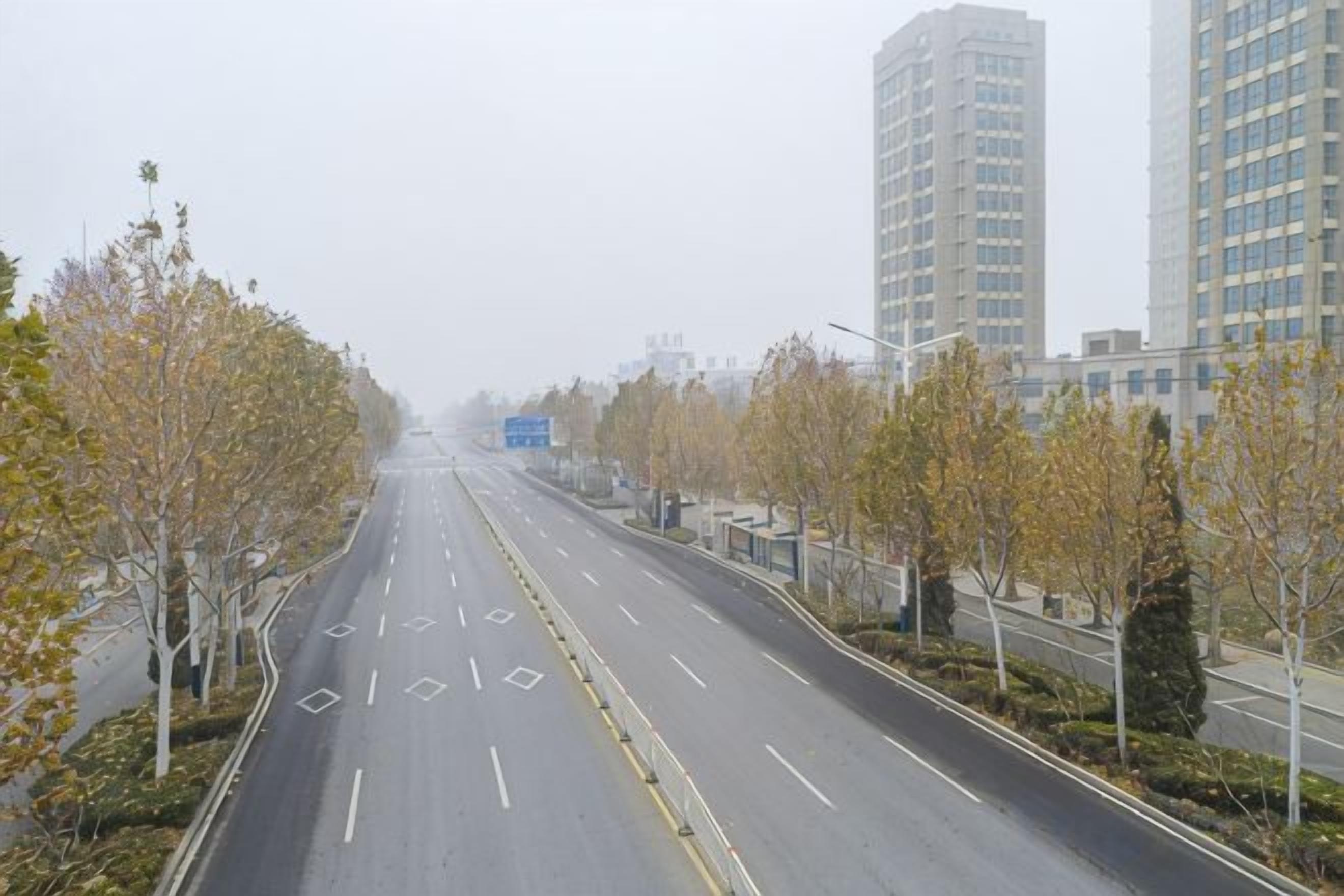 A multi-lane road with trees and buildings in the background.