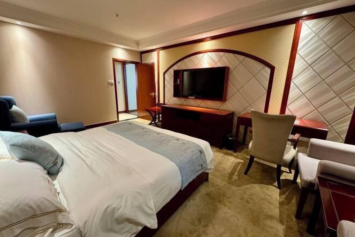 Een hotelkamer met een groot bed, een bureau, een stoel, een televisietoestel en een deur.
