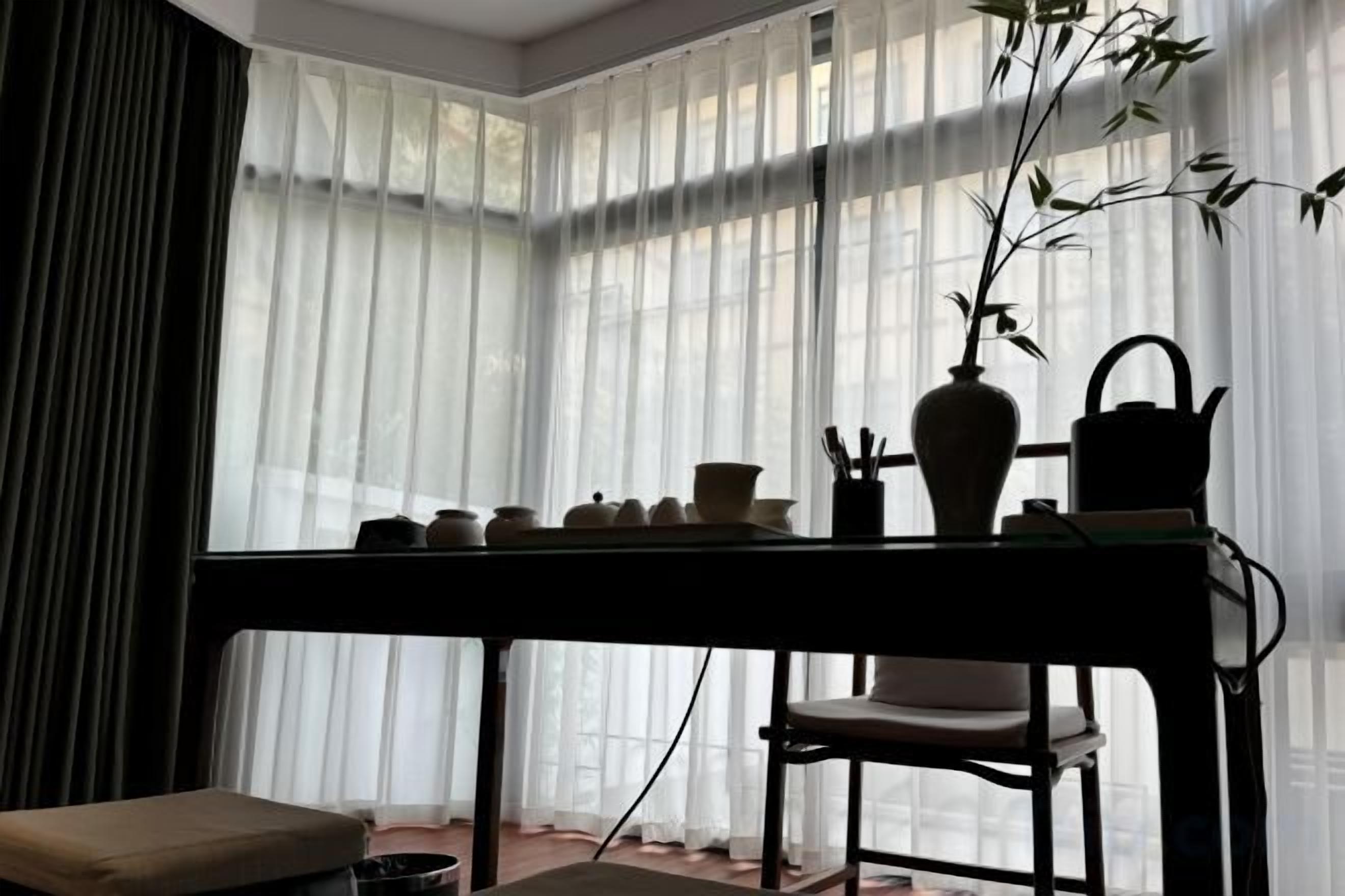 A room with a table set for tea, a chair, and a window with sheer curtains.