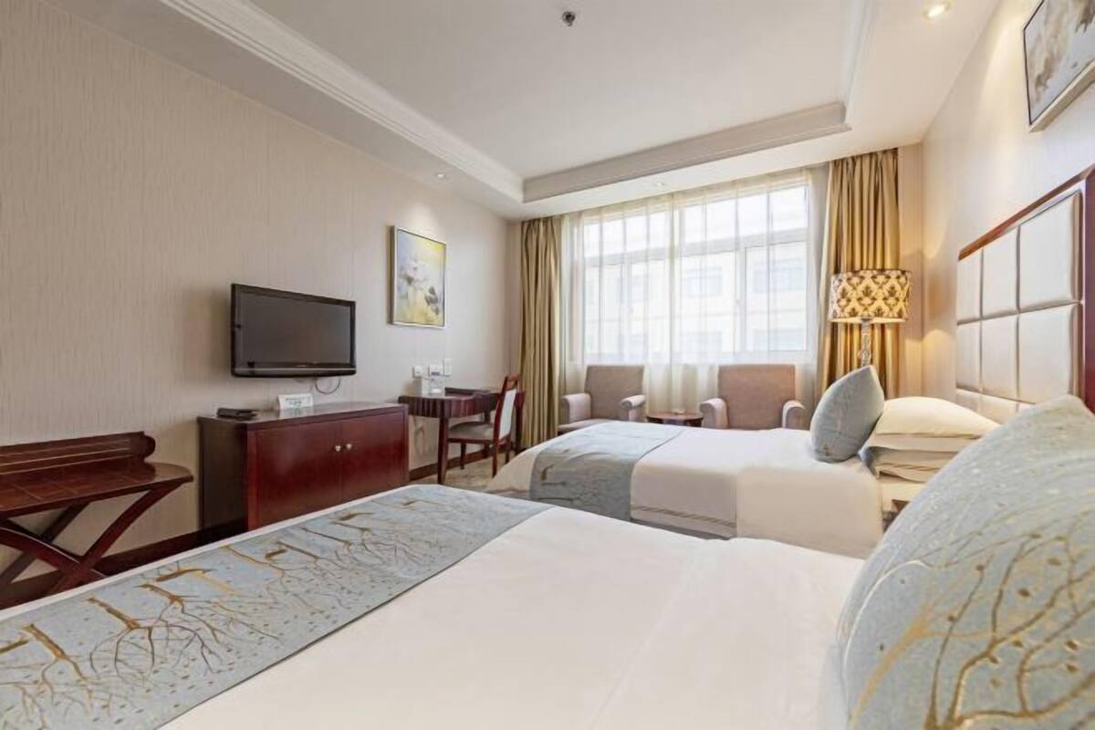 Een hotelkamer met twee bedden, een bureau, een televisie en een raam met gordijnen.