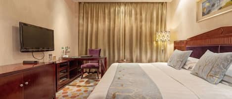 Ein Hotelzimmer mit einem großen Bett, einem Fernseher, einem Schreibtisch und einem Sessel.
