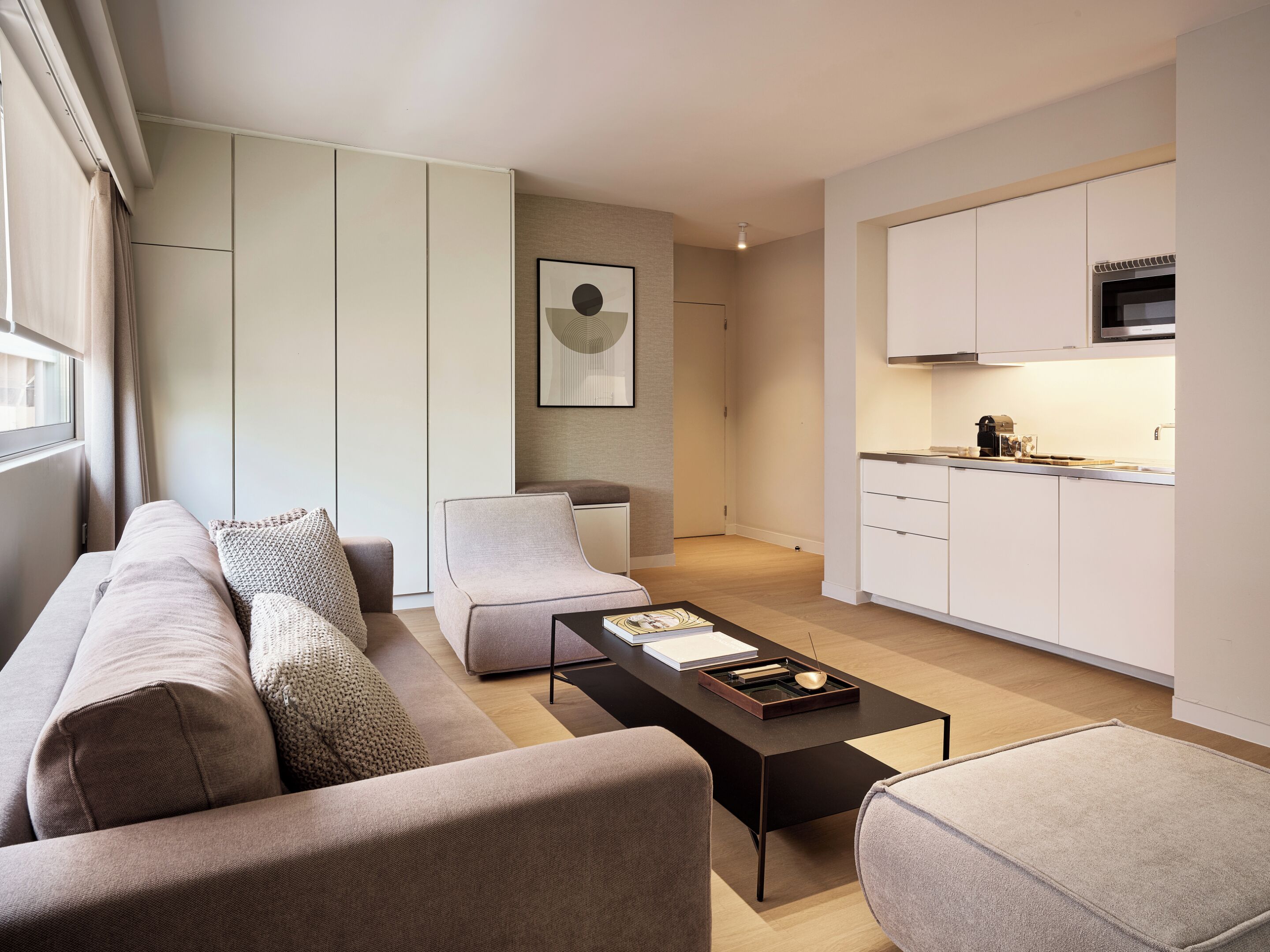 A modern living room with a sofa, a coffee table, and a kitchen area with cabinets and a microwave.